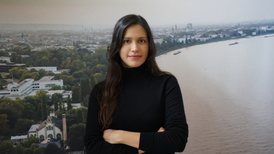 A female scientist in front of a wallpaper of the UN Bonn building on the Rhine.